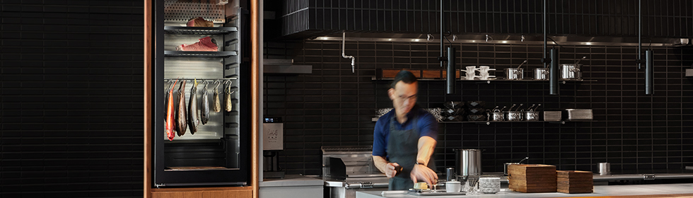 Koch in einer Restaurantküche neben einem DRY AGER Reifeschrank mit gereiftem Fisch.